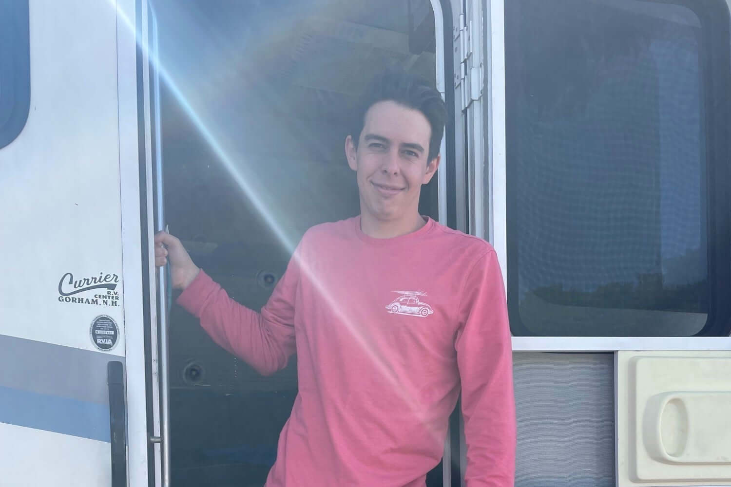Man in pink shirt and shorts standing in the doorway of a camper vehicle.