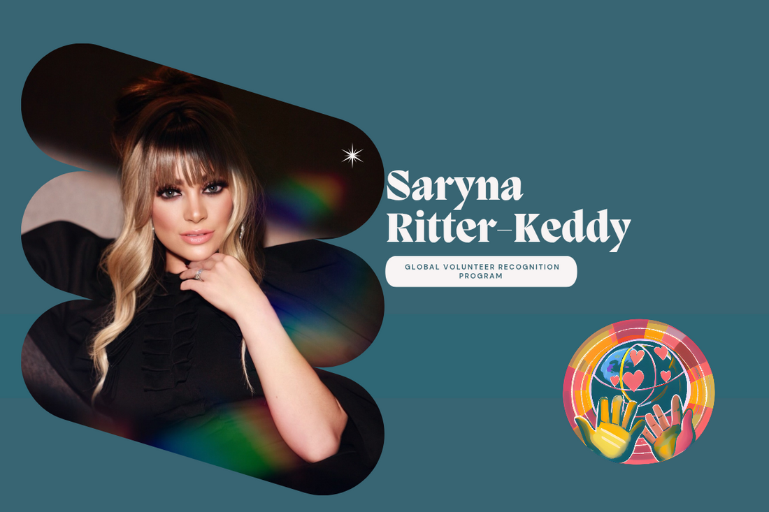 Saryna Ritter-Keddy  Woman with blonde hair and makeup, wearing a black top, with a blurred colorful background.