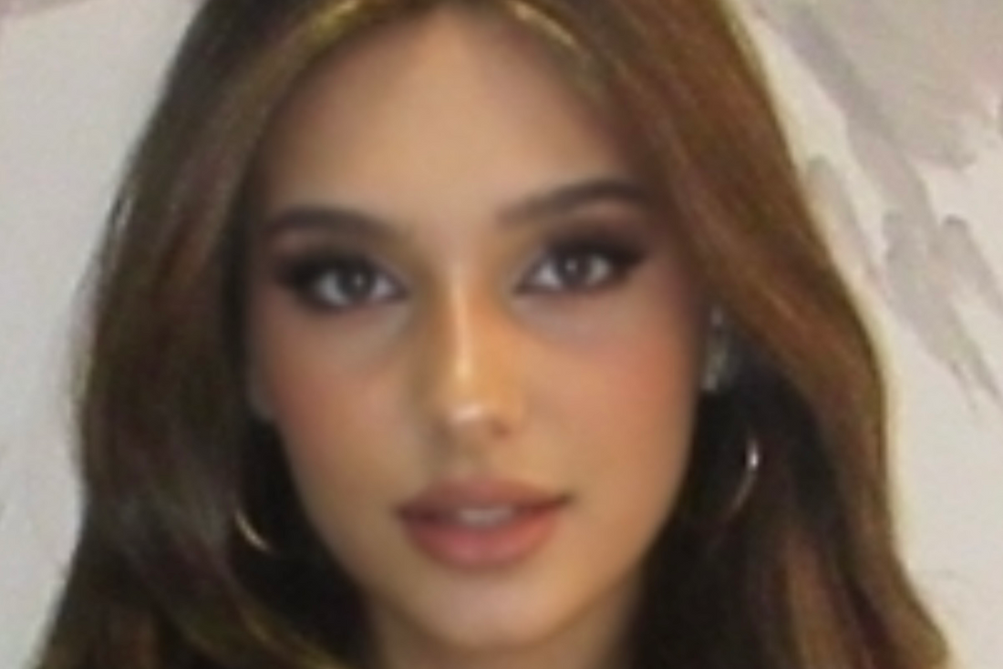 Close-up of a woman with long brown hair and makeup against a neutral background