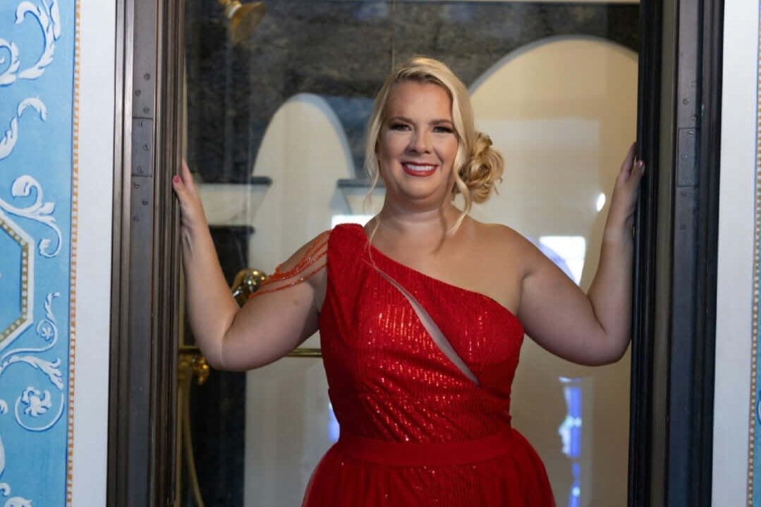 Laurel Barrett in a red dress standing in front of an ornate door.