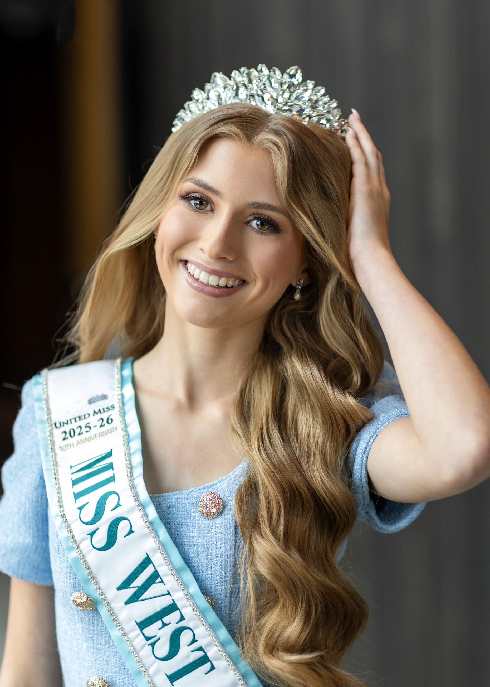 Woman wearing a tiara and 'Miss West' sash against a dark background