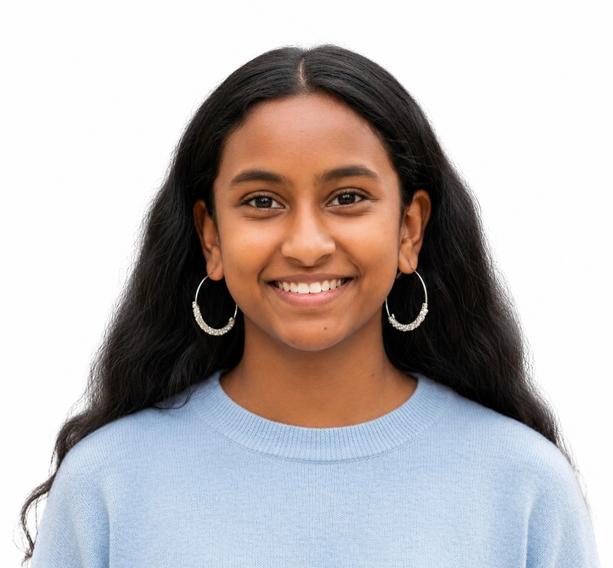 A smiling young woman with long dark hair wearing silver hoop earrings and a light blue sweater, photographed against a plain white background.