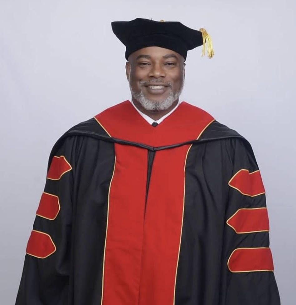 Person wearing a black and red graduation gown with a cap on a light gray background