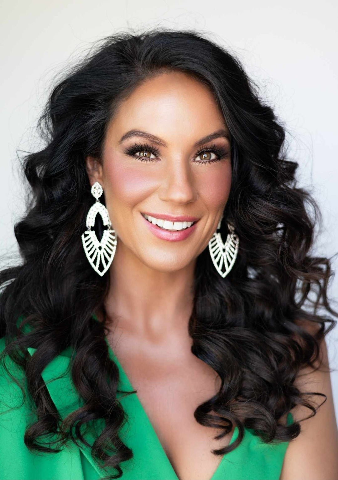 Woman with long, wavy black hair wearing large hoop earrings and a green top.