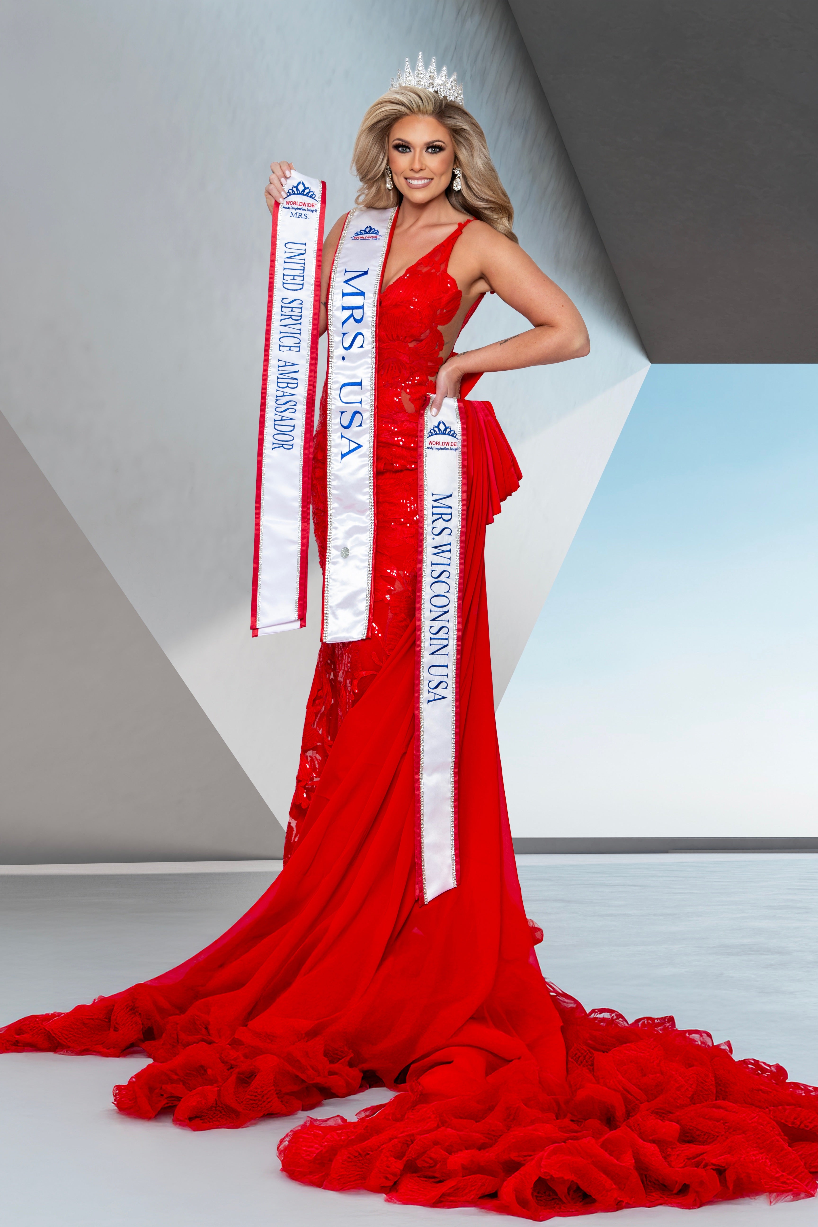 Woman in a red gown holding 'Mrs. USA' sashes against a light background