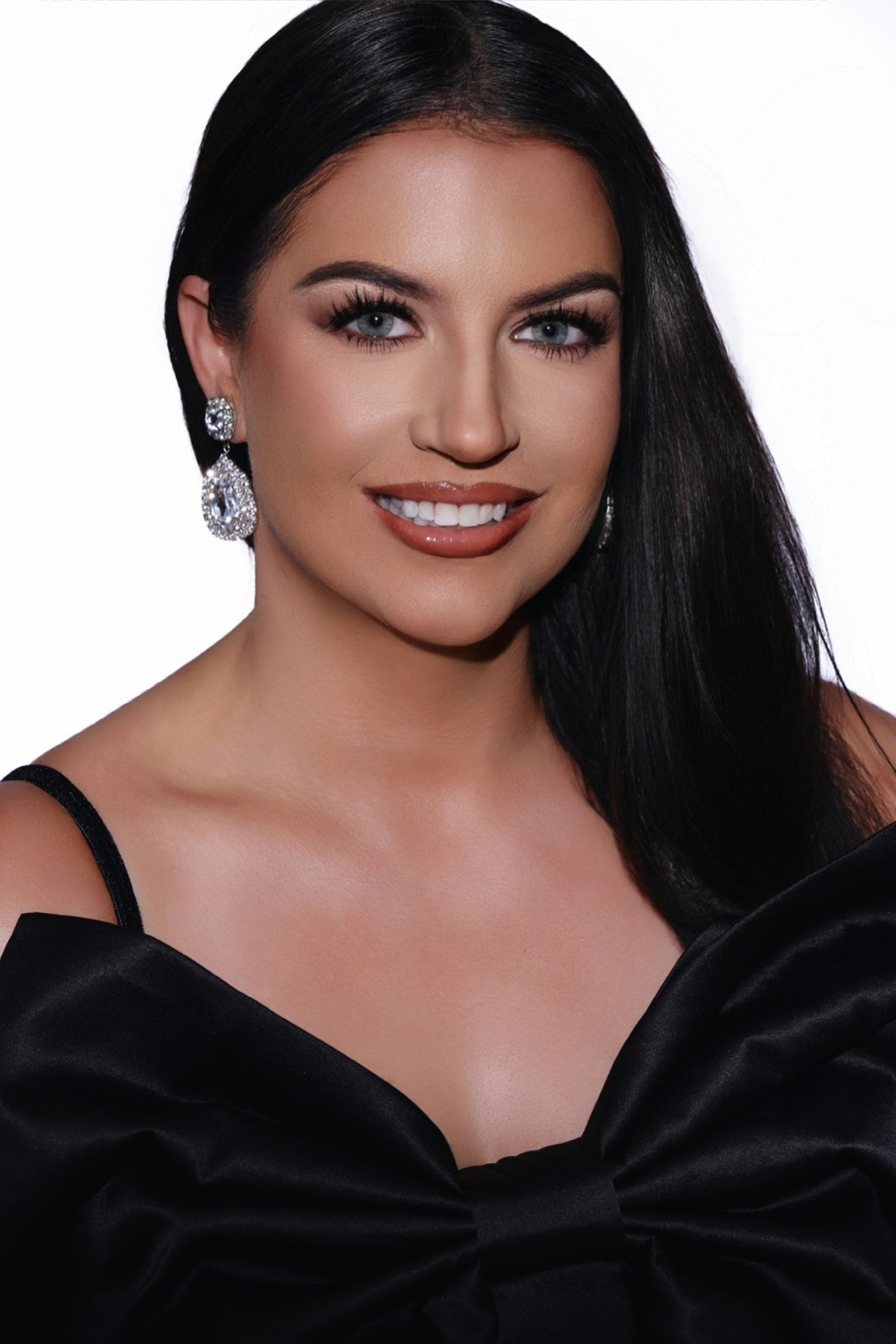 Woman wearing a black dress with a large bow, earrings, and makeup on a white background