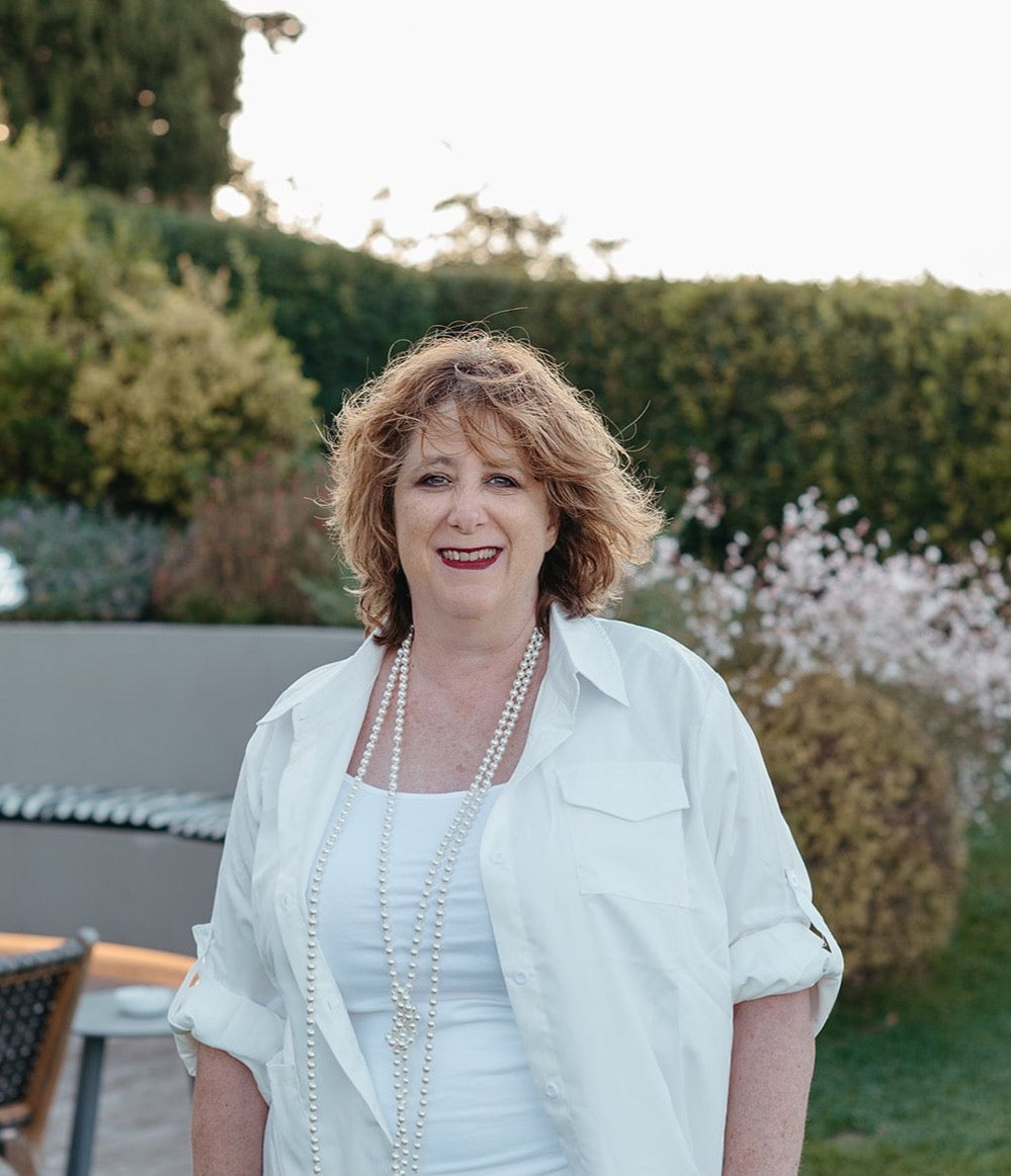 Woman standing outdoors with greenery and a fountain in the background