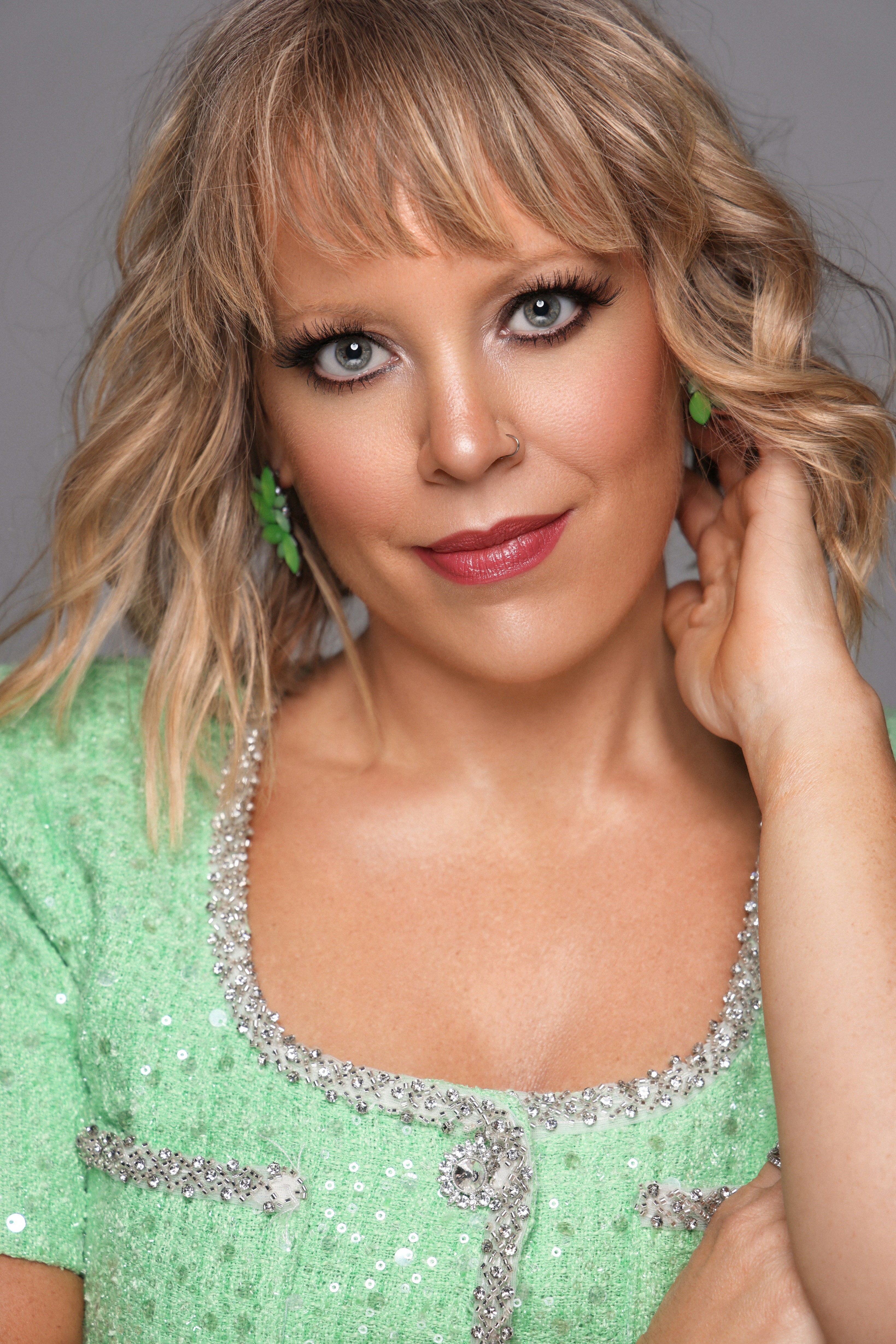 Woman in a green dress with sequin details posing against a gray background