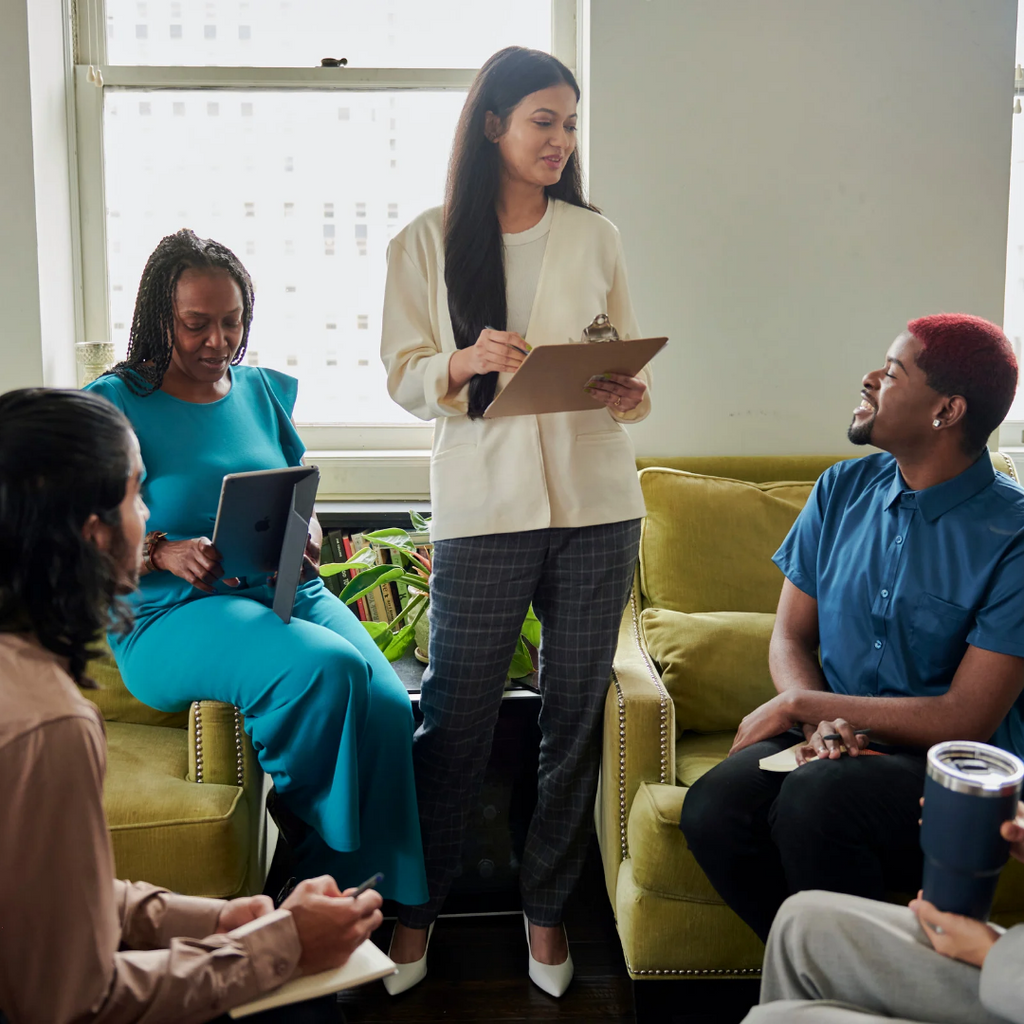 Group therapy session with a facilitator taking notes in a bright room.