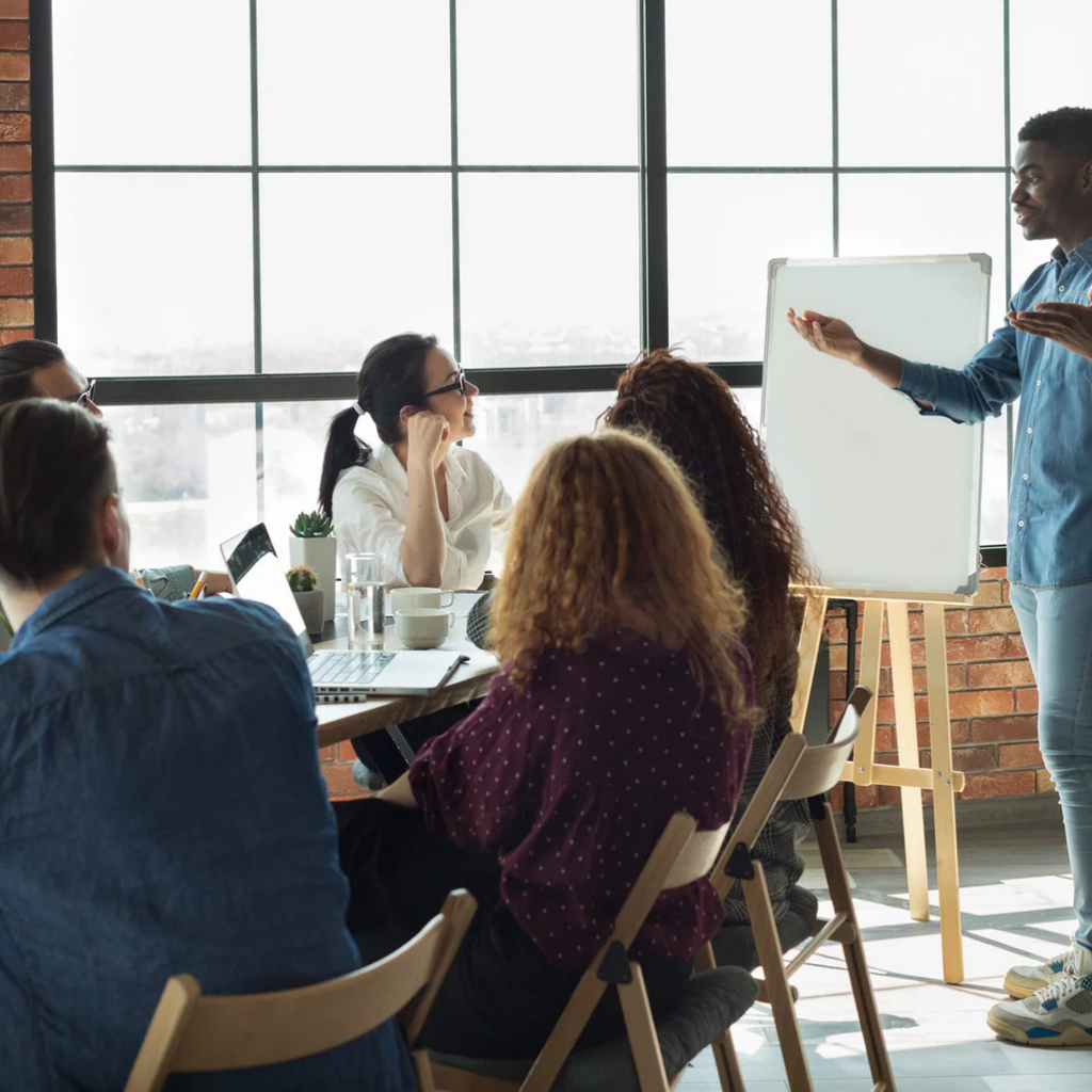 Group of people in a meeting room with a presenter using a whiteboard.