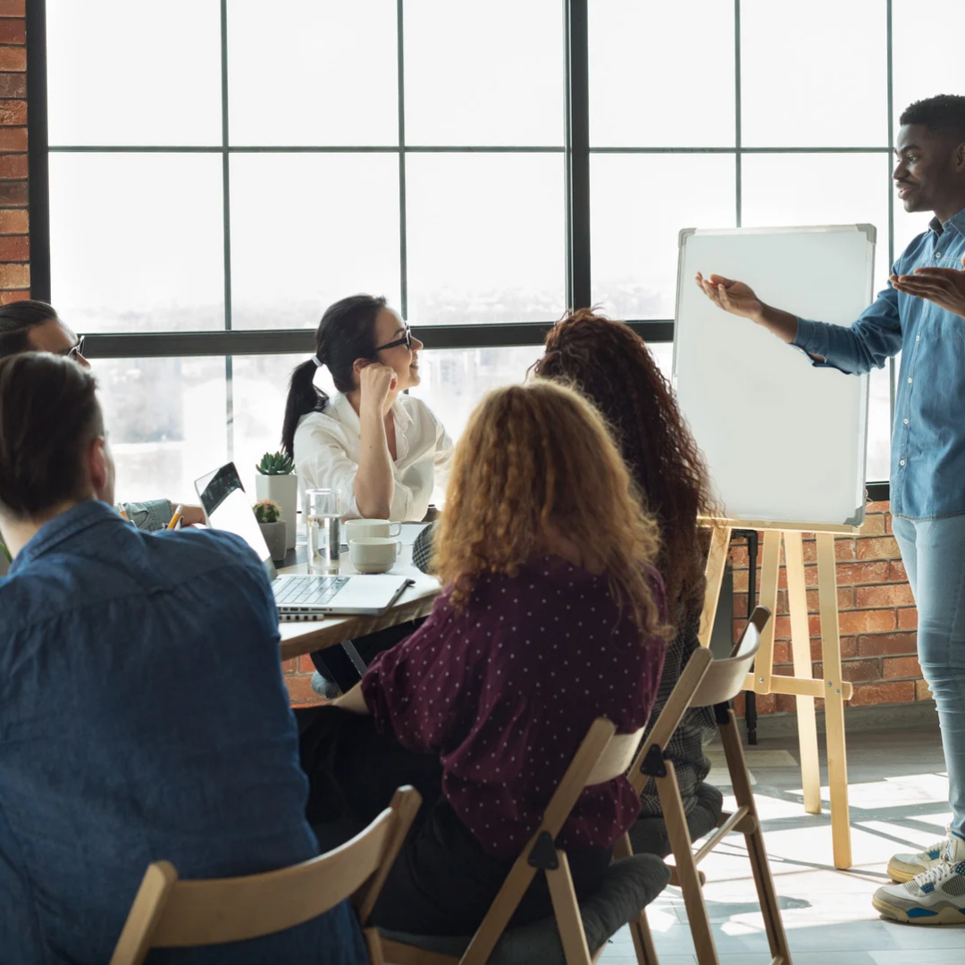 Group of people in a meeting room with a presenter using a whiteboard.